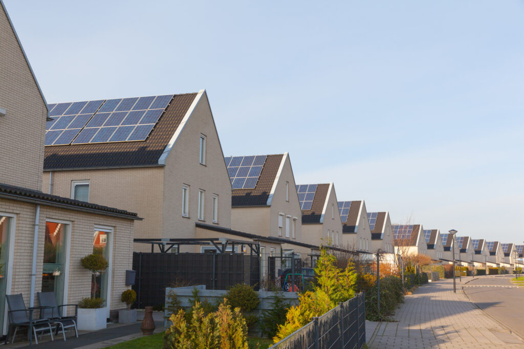 A row of houses in a neighborhood, all outfitted with solar panels on their roofs.