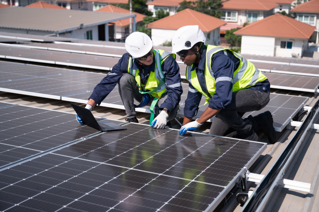 Two contractors in hi-visibility vests and hardhats installing a solar panel.